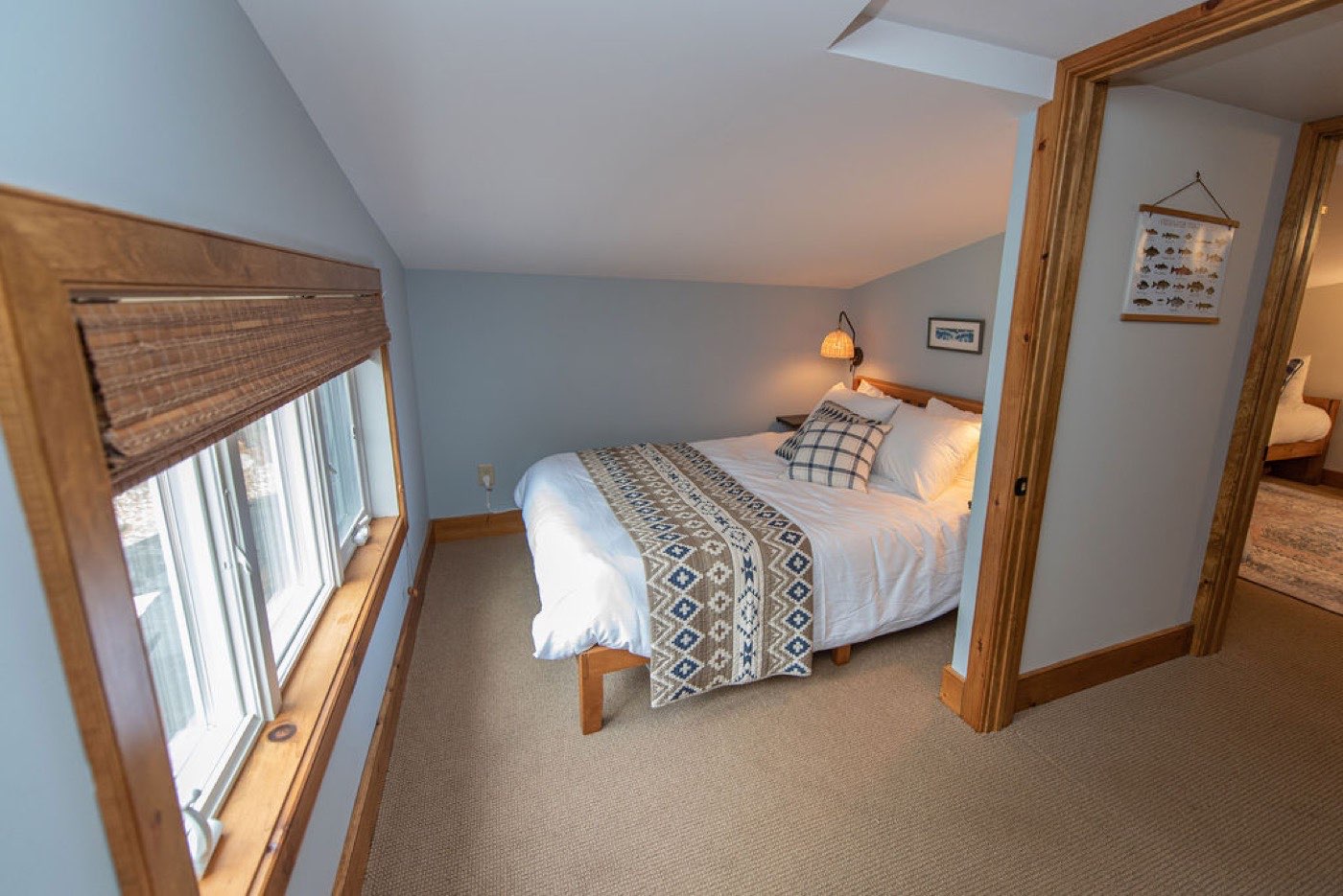 A bedroom in the guest house at Camp Sunnyside with a made bed, wool blanket, pine trim, and a fish-identification field chart on the wall.