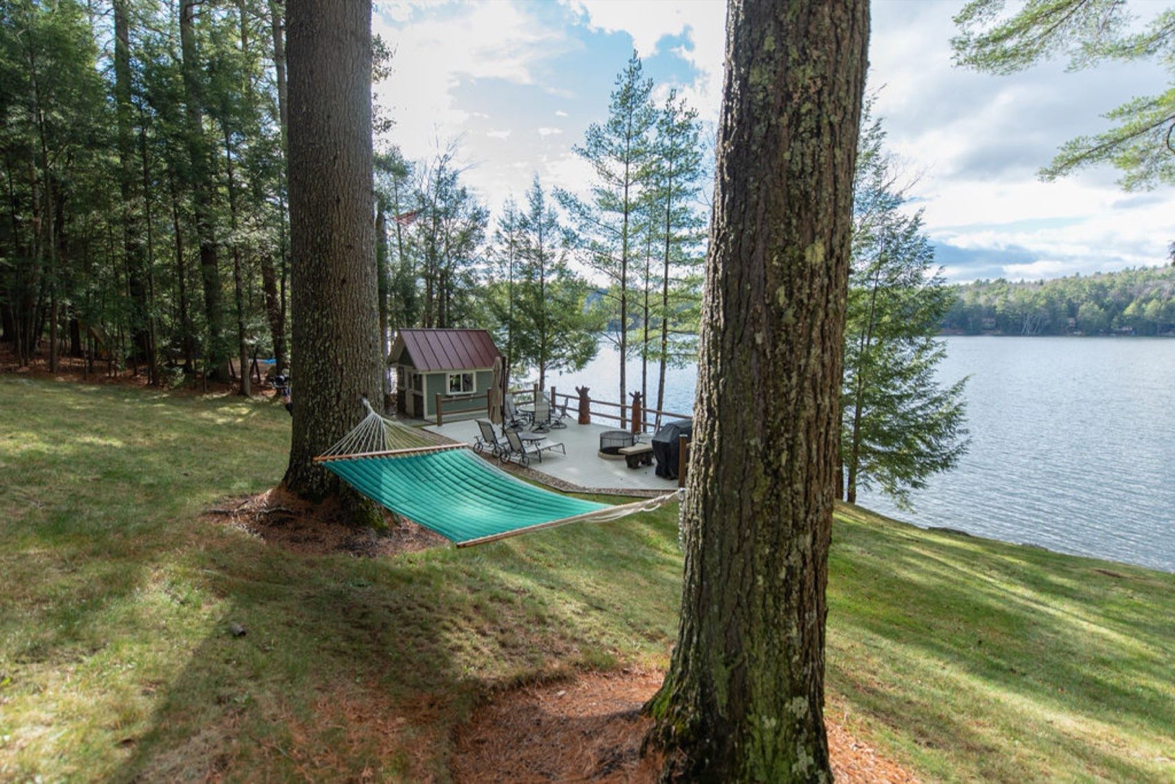 A hammock strung between two tall pines frames the lakeside deck, dock, and the blue expanse of Friends Lake at Camp Sunnyside.