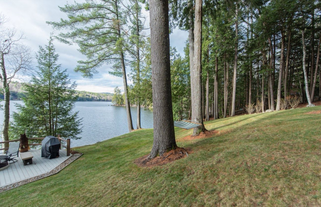 A hammock strung between two pines above the dock and Friends Lake at Camp Sunnyside on a clear summer day.